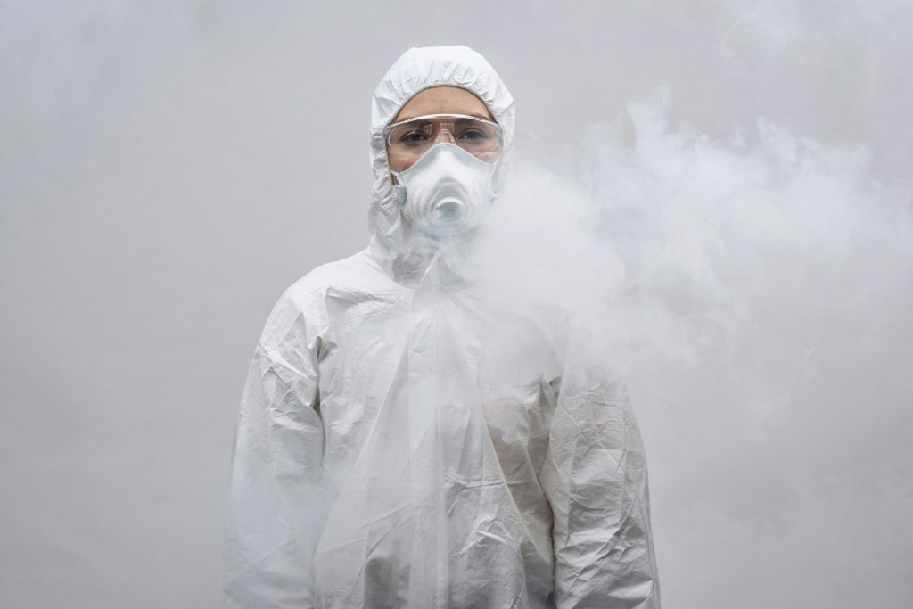 pexels-photo-4176924-4176924 Individual in protective suit and mask standing in smoke on white background.